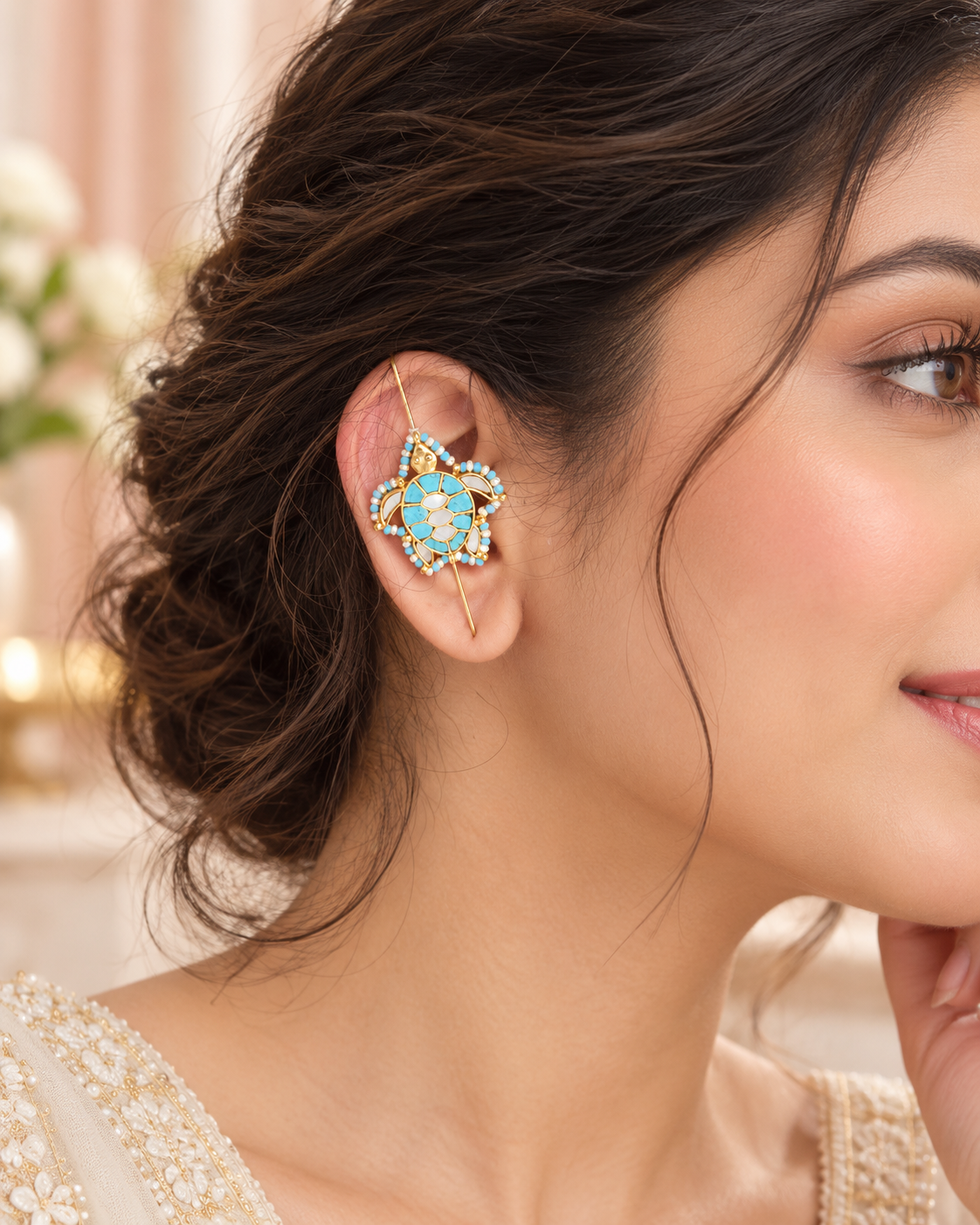 A close-up of a woman's ear wearing a gold-plated ear cuff decorated with light blue and white stones.