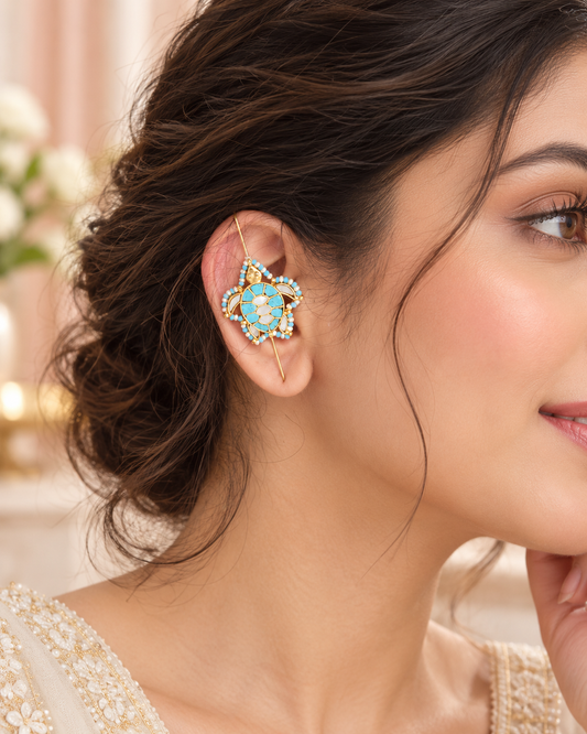 A close-up of a woman's ear wearing a gold-plated ear cuff decorated with light blue and white stones.